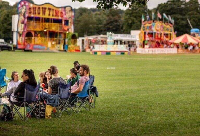 People sitting in a field by a fun fair