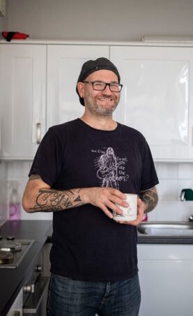 Dot Dot Dot guardian standing in their kitchen, holding a mug.